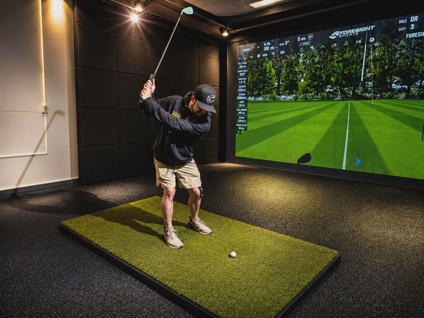 Golf simulator setup inside Cleveland Fitness Club with screen display and synthetic turf hitting mat